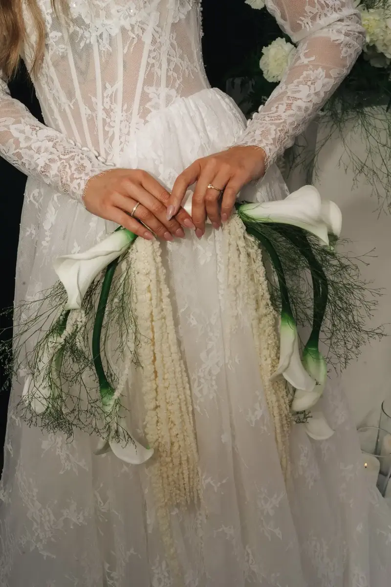 Hände der Braut mit Ringen und Calla-Strauß auf Spitzenkleid